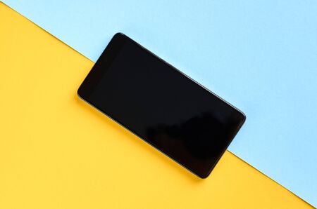 Black cellphone on yellow and blue background composition, mobile phone. Flat lay and top view photoの写真素材