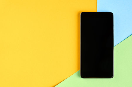 Black cellphone on yellow and blue background composition, mobile phone. Flat lay and top view photo