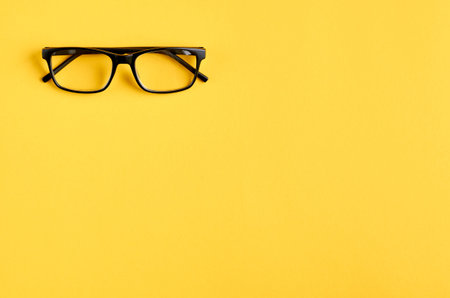 Black glasses on yellow background composition, eyeglasses. Flat lay and top view photo