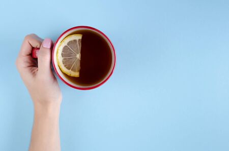 Hand with red tea cup and lemon slice composition on blue background. Flat lay, layout and tabletop mockup with copy space.の写真素材