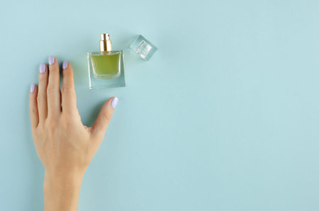 Hand with perfume bottle composition on blue background. Flat lay, layout and tabletop mockup with...