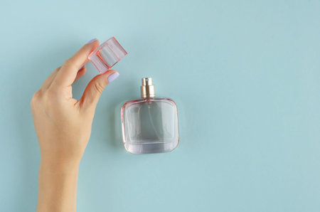 Hand with perfume bottle composition on blue background. Flat lay, layout and tabletop mockup with...
