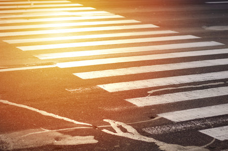 Zebra pedestrian crossing. Patched asphalt. Not a very safe crossing over a wide road. Sunlight.
