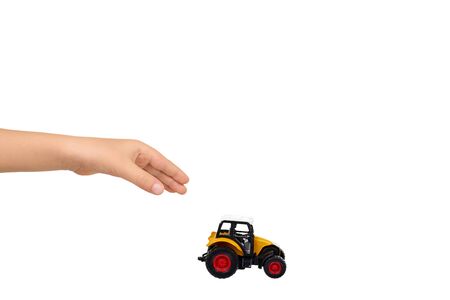 Kids hand with yellow plastic traktor toy. Farming vehicle, harvest equipment. Isolated on white background. Copy space.の写真素材