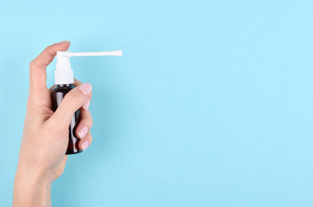 Hand with throat spray bottle on blue background. Flat lay, overhead view image.