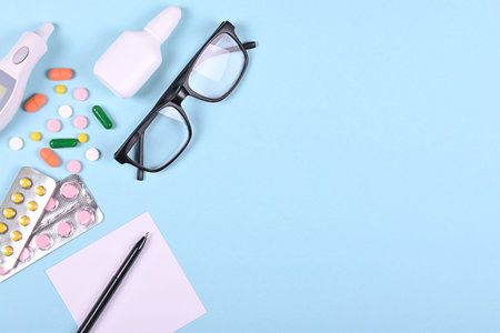 Medical pills, thermometer, eyeglasses and spray bottle on blue background, flat lay, overhead view image. Medicine concept.の写真素材