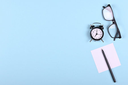 Black glasses, clock, paper and pen on blue background composition. Flat lay, overhead view image.の写真素材