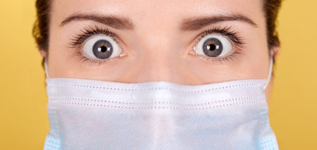 Portrait of a brunette girl with scary eyes in a medical mask, wide open eyes with horror. Isolated...