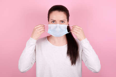 Portrait of a brunette girl, puts on a medical mask. Isolated on pink background.の写真素材