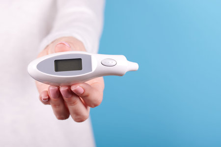Electronic thermometer in hands on a blue background. Close up photo.