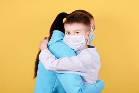 Portrait of a brunette boy and his mother, lovely hugs, kid is looking to the camera. Isolated on yellow background.の写真素材