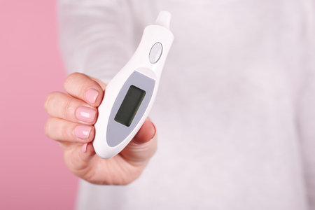 Electronic thermometer in hands on a pink background. Close up photo.