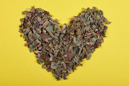 Dried basil leafs macro photo, herb seasoning. Heart shape. Isolated on yellow background.の写真素材