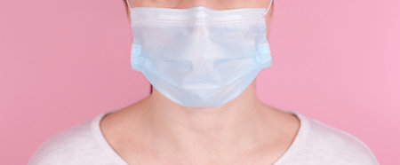 Portrait of a brunette girl in a medical mask. Isolated on pink background, banner.