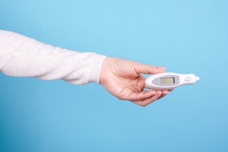 Electronic thermometer in hands on a blue background.
