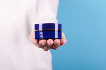 Cream in jar in hand on blue background.