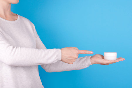 Cream in jar in hand on blue background.