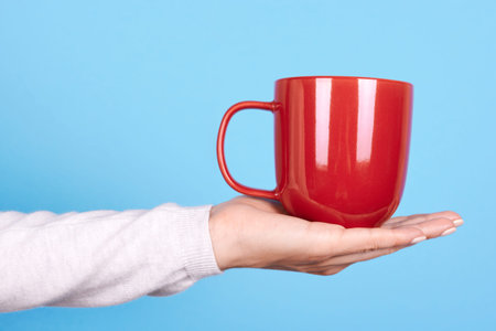 Hand with red mug with handle.
