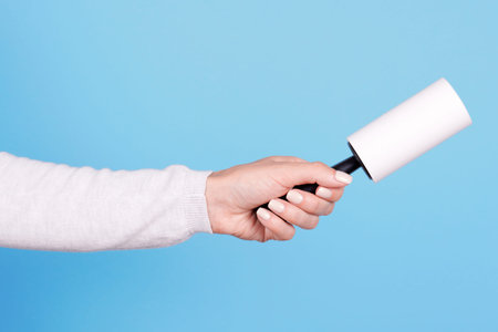 Hand with sticky roller for cloth cleaning.