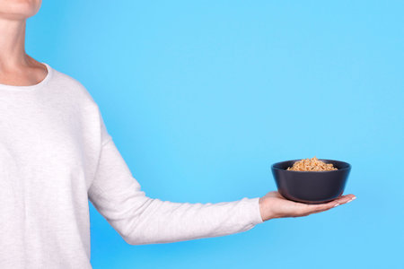 Hand with asian instant noodle in dark bowl.