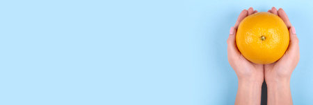 Hand with ripe and fresh orange fruit on blue background.の写真素材