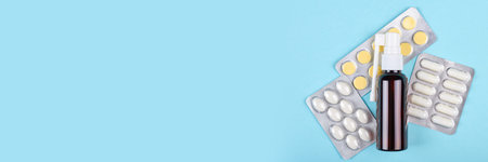 Throat spray bottle and pills on blue background.