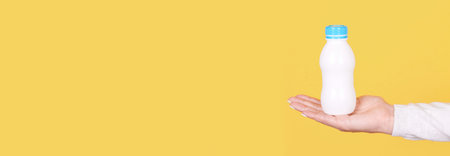 White bottle with kids yogurt in hand, isolated on yellow background, copy space template, banner.