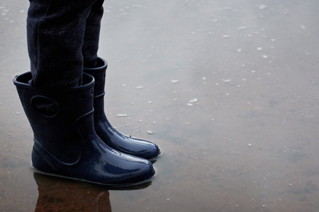 Childs legs in boots stand in puddle.