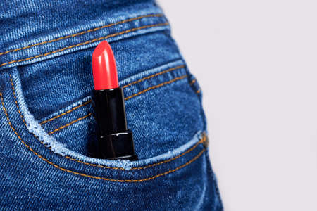 Red lipstik in jeans pocket on grey.の写真素材