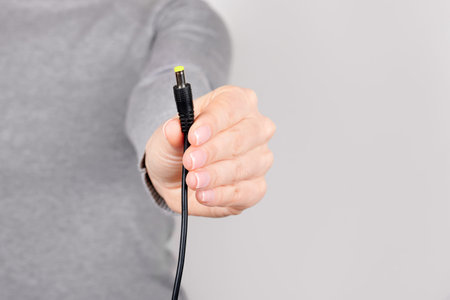 Hand with black power plug on grey.