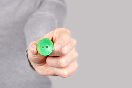 Hand with green sewing button on grey.の写真素材
