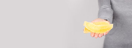 Hand with dried mango snack on grey.