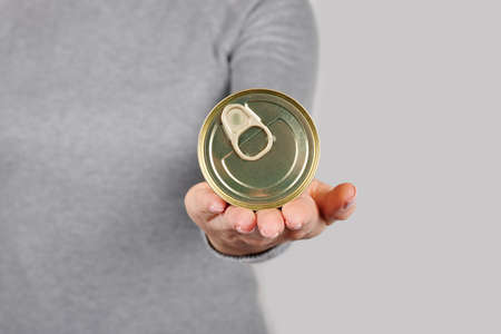 Hand with metal can, preserve tin on greyの写真素材
