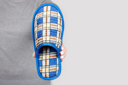 Hand with textile home slippers on grey