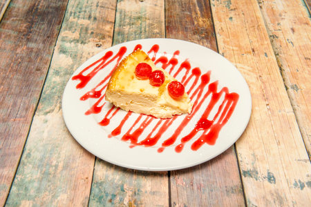 Portion of cheesecake with candied plums and strawberry syrup on white plate