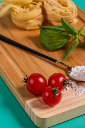 Image of cherry tomatoes in the foreground on a bamboo table with flour, basil and pasta in the background, all on a green backgroundの写真素材