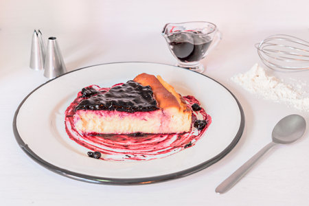Cheesecake portion on enameled metal plate on white background accompanied by flour, bars, jam jar and spoonの写真素材