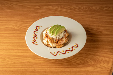 Arepa on a plate with shredded meat, grated cheese, avocado and mayonnaise sauce on oak wood tabl