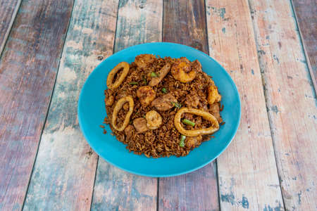 Oriental rice dish with seafood and vegetables on blue plate and wooden tableの写真素材