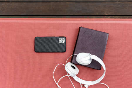 overhead view of white headphones, vintage book and smartphone on a deck hammock for a relaxing momentの写真素材