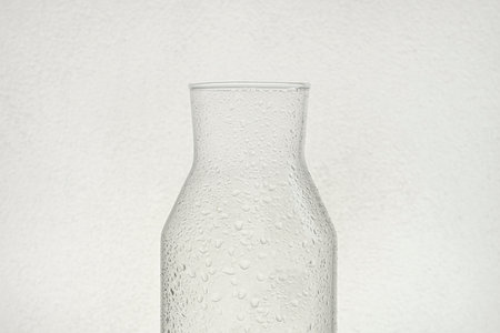 Backlit transparent glass half bottle and water drops on its surface with white background.の写真素材