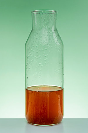 Tea Half full glass bottle on green table and backlit green backgroundの写真素材