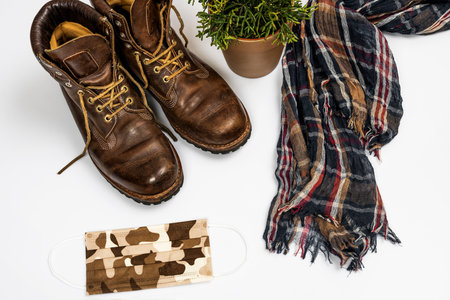 Top view image of brown leather hiking boots with scarf, plant and camouflage mask on white backgroundの写真素材