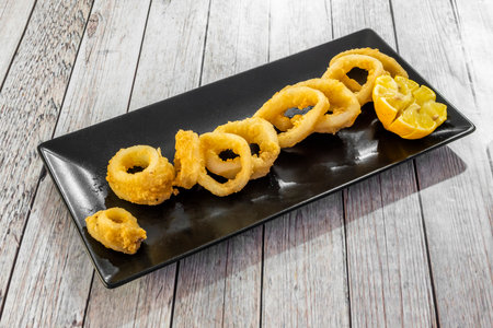 Tapa of battered squid sliced into rings on a black plate with sliced lemonの写真素材