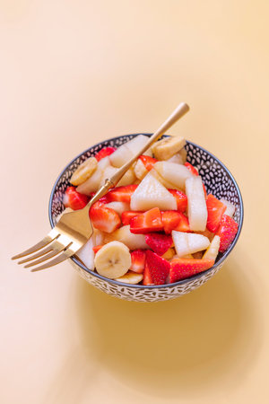 bowl with chopped fruits and golden fork on top on yellow backgroundの写真素材