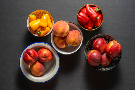Various bowls of nectarines, peaches and yellow and other red peppers on black backgroundの写真素材