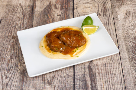 Rectangular white plate of braised cheeks on bed of mashed potatoes on top of gray tableの写真素材