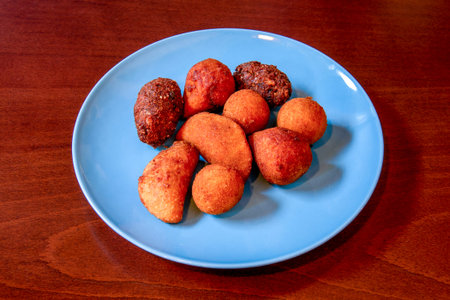 Blue plate with croquettes of different flavors and shapes on reddish wooden table