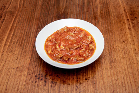 White plate with chunks of stewed meat in Spanish sauce on wooden tableの写真素材