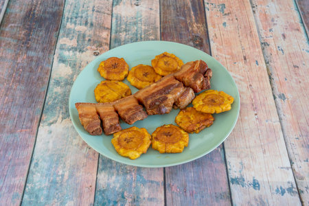 Typical Colombian recipe for chicharron garnished with fried plantain slices on a blue plateの写真素材